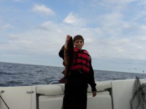 A young man holds up a fish he caught in the spring during a trip with Morning Flight Charters